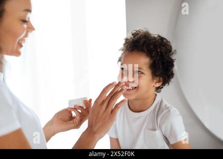 Sourire jeune garçon obtenir une crème appliquée sur son visage Banque D'Images