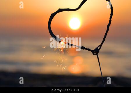 Étincelant en forme de coeur brûlant sur fond de mer et soleil levant à l'aube. Feu du Bengale en forme de coeur scintillant à l'aube du lever du soleil et au coucher du soleil sur la mer. Amour engouement Saint-Valentin Banque D'Images