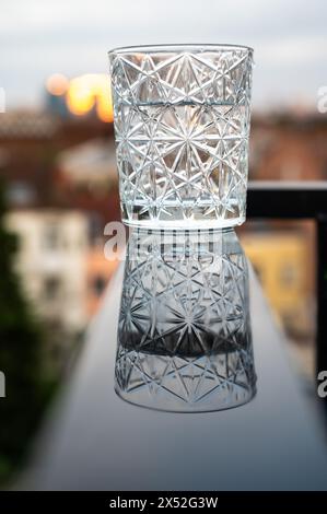 Verre d'eau avec design de cristal de luxe reflétant sur une surface noire humide, Bruxelles, Belgique Banque D'Images