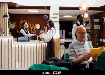 Femme caucasienne senior debout au comptoir du hall de l'hôtel et s'enregistre avec passeport. Concierge femme au bureau d'enregistrement retournant le document personnel de la vieille voyageuse après vérification de l'identité. Banque D'Images