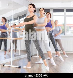 Femme exécutant le tendu de combat à la barre de ballet à la classe de groupe de débutants Banque D'Images
