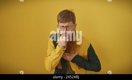 Un homme barbu rousse dans des lunettes toussant sur fond jaune. Banque D'Images