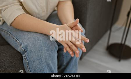 Gros plan des mains serrées d'une jeune femme dans un cadre de maison détendu, dénotant le calme et le confort. Banque D'Images