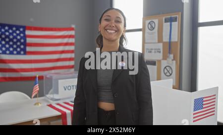 Une jeune femme hispanique souriante avec un autocollant «j'ai voté» se tient dans un centre de vote avec des drapeaux américains. Banque D'Images