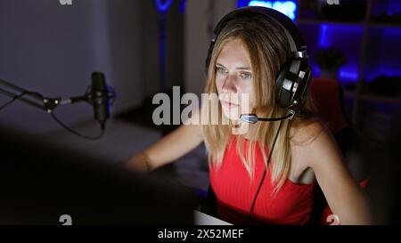 Femme concentrée diffusant dans une pièce sombre avec microphone et casque de jeu la nuit. Banque D'Images