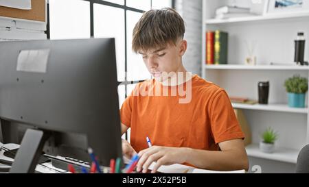 Adolescent concentré étudiant dans une installation de bureau à domicile moderne, avec un ordinateur et des ordinateurs portables Banque D'Images