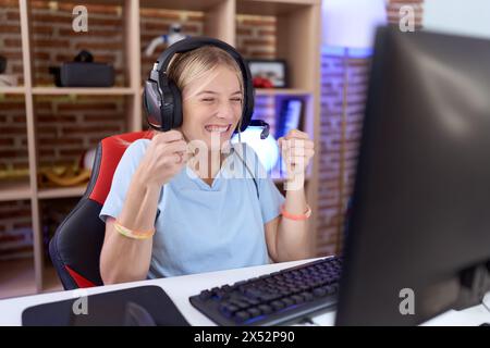 Jeune femme caucasienne jouant à des jeux vidéo portant des écouteurs excités pour le succès avec les bras levés et les yeux fermés célébrant la victoire en souriant. gagnant Banque D'Images