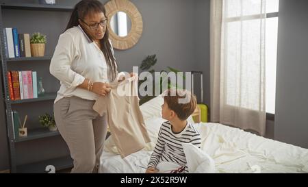 Mère et fils pliant le linge ensemble dans une chambre confortable et bien éclairée, incarnant un moment familial chaleureux. Banque D'Images