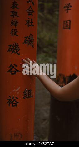 La marche révérencieuse de la jeune femme, marchant et touchant les portes torii traditionnelles japonaises à fushimi inari-taisha, un regard en arrière alors qu'elle se déplace le long du o Banque D'Images