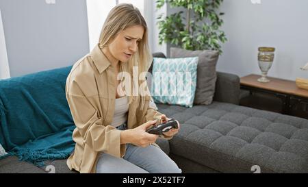 Attrayante jeune femme blonde englouti dans une intense session de jeu en ligne, assise confortablement sur son canapé accueillant, totalement perdu dans le monde de digi Banque D'Images