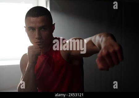 Jeune homme sérieux avec les poings serrés concentrant l'attention sur rival ou punching sac tout en pratiquant des coups de pied de base et des techniques de défense Banque D'Images