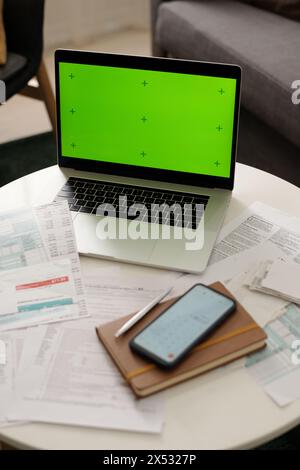 Angle élevé de l'ordinateur portable avec la touche chroma sur l'écran debout sur la table avec les factures impayées et les papiers financiers, bloc-notes et smartphone Banque D'Images