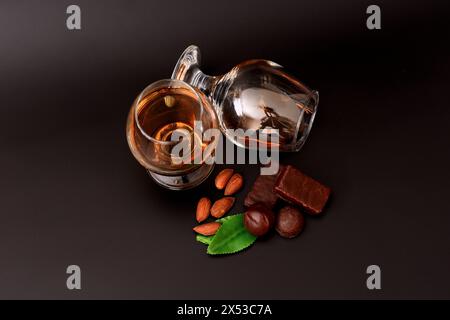 Deux verres de cognac sur fond noir, à côté d'une amande, de feuilles de menthe et de chocolats. Vue de dessus, pose à plat. Banque D'Images