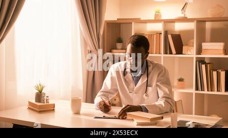 Le mode de vie des médecins. Carrière médicale. Profession professionnelle. Médecin masculin occupé confiant en manteau blanc travaillant la prescription d'écriture à l'intérieur moderne léger avec l'espace libre. Banque D'Images