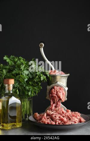 Hachoir à viande manuel avec viande hachée de bœuf, huile et persil sur table grise Banque D'Images