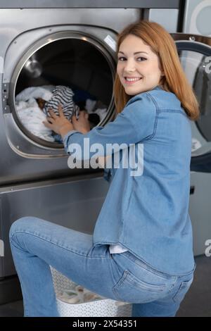 femme heureuse mettant des vêtements dans la machine à laver pour la lessive Banque D'Images