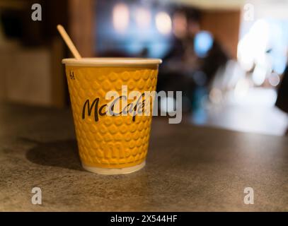 Tasse à café McCafe en papier jaune avec bâtonnet en bois sur le comptoir en pierre du restaurant McDonald's. Banque D'Images