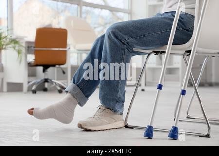 Jeune homme blessé après accident avec béquilles assis en clinique Banque D'Images