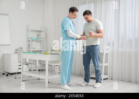 Nutritionniste masculin mesurant la taille de l'homme en clinique Banque D'Images