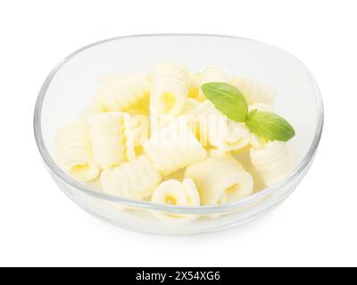 Savoureuses boucles de beurre et feuilles de basilic dans un bol isolé sur blanc Banque D'Images