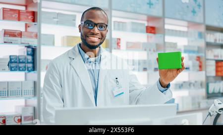 Pharmacie Drugstore : Portrait de pharmacien professionnel noir tenant Green Mock-up Template Medicine Package, regardant la caméra, souriant. Spécialiste recommandant le meilleur produit Banque D'Images