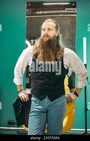 Homme Bearded portrait de barbier . Mâle jeune barbier européen barbier joyeux barbu aux cheveux longs, debout avec des ciseaux de coupe de cheveux dans des biscuits et souriant Banque D'Images