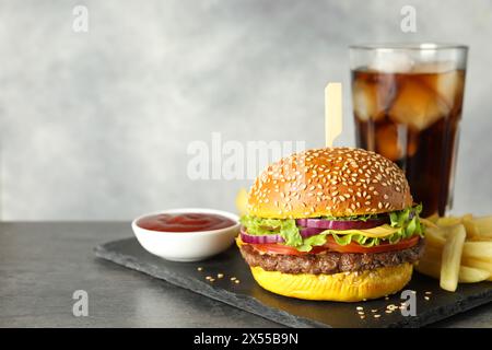 Hamburger avec délicieuse patty, boisson gazeuse, frites et sauce sur table sombre sur fond gris, espace pour le texte Banque D'Images