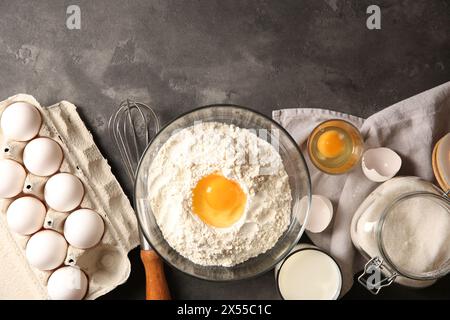 Faire de la pâte. Farine avec jaune d'oeuf dans un bol et d'autres produits sur une table texturée grise, pose à plat Banque D'Images