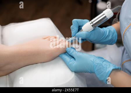 Pédicure pratiquant une pédicure matérielle à une femme, en utilisant une perceuse à ongles Banque D'Images