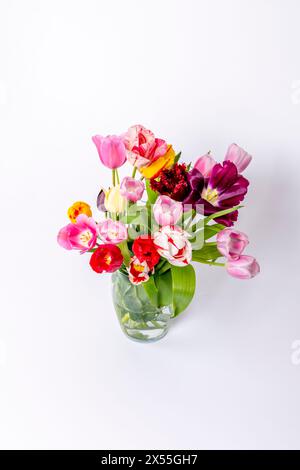 Un vase rempli d'une variété de fleurs colorées, y compris des tulipes roses, jaunes et rouges, assis sur une table blanche. Banque D'Images