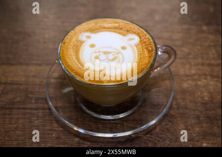 Délicieuse tasse de cappuccino avec latte art visage d'ours, servi dans un verre transparent sur une surface en bois Banque D'Images