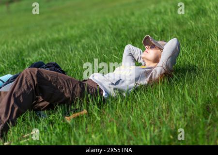 Jeune femme touristique prenant un repos sur la colline verte couchée dans l'herbe verte. Banque D'Images