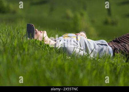 Jeune femme touristique prenant un repos sur la colline verte couchée dans l'herbe verte. Banque D'Images