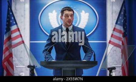 Représentant d'une jeune organisation prenant la parole lors d'une conférence de presse dans le bâtiment du gouvernement. Attaché de presse prononçant un discours au Sommet. Ministre s'adressant au Congrès. Toile de fond avec drapeaux américains. Banque D'Images