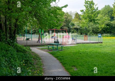 Une petite aire de jeux pour enfants vide et colorée entourée d'arbres, d'arbustes et de fleurs printanières. Banque D'Images