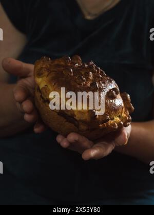 Gros plan vertical des mains d'une femme tenant un pain festif ukrainien sucré traditionnel fait maison sur un fond sombre. Pain légèrement plié Banque D'Images
