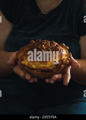Gros plan vertical des mains d'une femme tenant un pain festif ukrainien sucré traditionnel fait maison sur un fond sombre. Banque D'Images