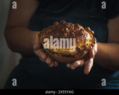 Gros plan horizontal des mains d'une femme tenant un pain festif ukrainien sucré traditionnel fait maison sur un fond sombre. Banque D'Images