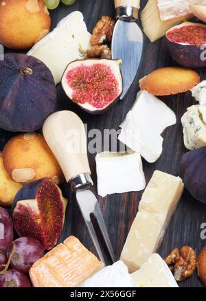 Assiette à fromage gourmet avec brie, roquefort et camembert, figues et couteaux à fromage en gros plan sur planche en bois Banque D'Images