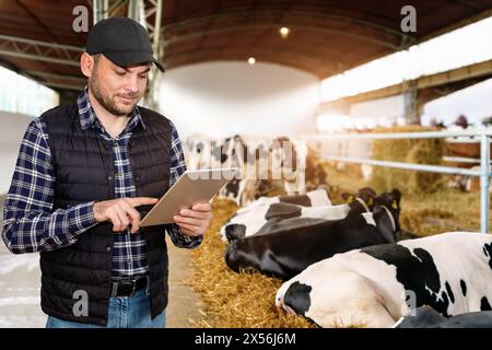 Homme agriculteur moderne travaillant sur sa tablette numérique dans la ferme d'élevage. Banque D'Images