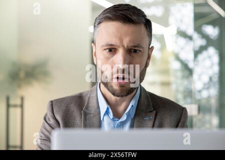 Un homme d'affaires professionnel se concentre profondément tout en travaillant sur son ordinateur portable dans un environnement de bureau contemporain bien éclairé. Il semble englouti et sérieux. Banque D'Images