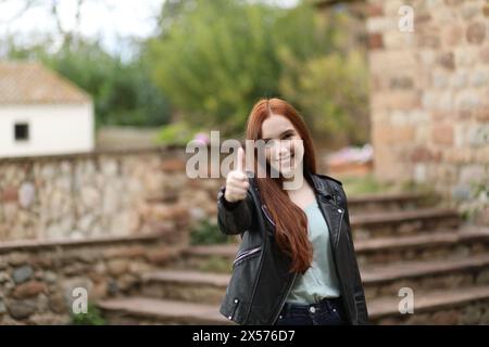 Jeune femme aux cheveux longs sourit levant le bras et faisant un geste de pouce levé Banque D'Images