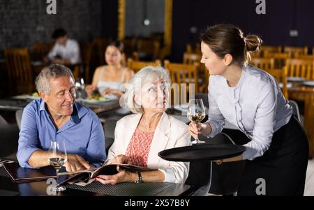 Serveuse apportant l'apéritif à un couple de personnes âgées en sélectionnant des plats dans le menu Banque D'Images