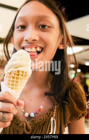 La fille adolescente d'Asie du Sud-est aime manger un cône de crème glacée à la vanille au centre commercial Banque D'Images