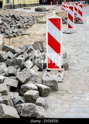 Pavage de rues avec pavés historiques en granit martelé, restauration de la surface des rues de la ville, cubes de roches, signalisation verticale rayée rouge et blanche Banque D'Images