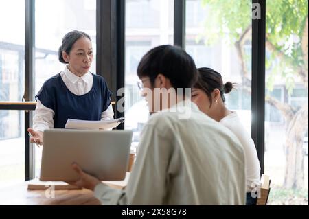 Une professeure asiatique expérimentée et professionnelle ou enseignante enseigne à ses élèves dans la salle de classe, expliquant et aidant ses élèves w Banque D'Images