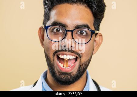 Homme de médecin indien souriant met de comprimé pilule vitamine D ou oméga-3 capsule jaune dans la bouche, recommande des médicaments de traitement de guérison d'immunisation. Les soins de santé. Pharmacien apothicaire sur fond beige Banque D'Images