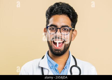 Sourire indien docteur homme hindou met de pilule de comprimé capsule blanche dans la bouche, recommande le traitement de cure d'immunisation de médicaments. Les soins de santé. Vitamines pour les articulations, les cheveux, la peau, les ongles. Pharmacien apothicaire Banque D'Images