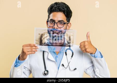 Jeune médecin indien orthodontiste examine une image panoramique de radiographie des dents de la mâchoire. Modèle 3D de la bouche du patient, IRM. Dentisterie, soins bucco-dentaires. Homme stomatologique arabe sur fond beige Banque D'Images