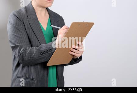 Gros plan d'une femme en veste grise écrivant sur un presse-papiers, fond de studio vide gris Banque D'Images
